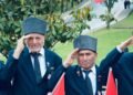 Two elderly veterans saluting during an outdoor ceremony with flags in Balıkesir, Türkiye.