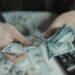Close-up of hands counting hundred dollar bills with a calculator in the background.